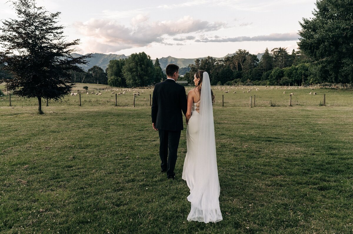 bride and groom holding hands and walking away from camera on lawn at orton bradley park wedding with ocean and mountains in background at sunset