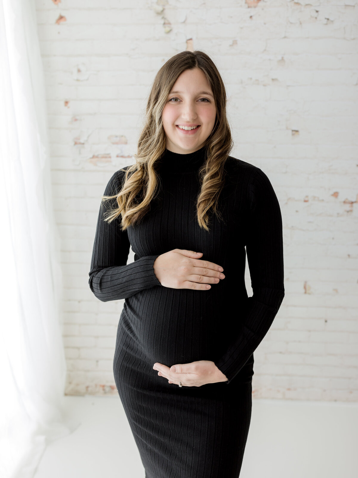 pregnant mother in black maternity dress holding baby bump for maternity photoshoot