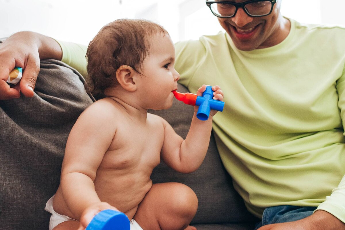 A dad plays with his baby on the couch