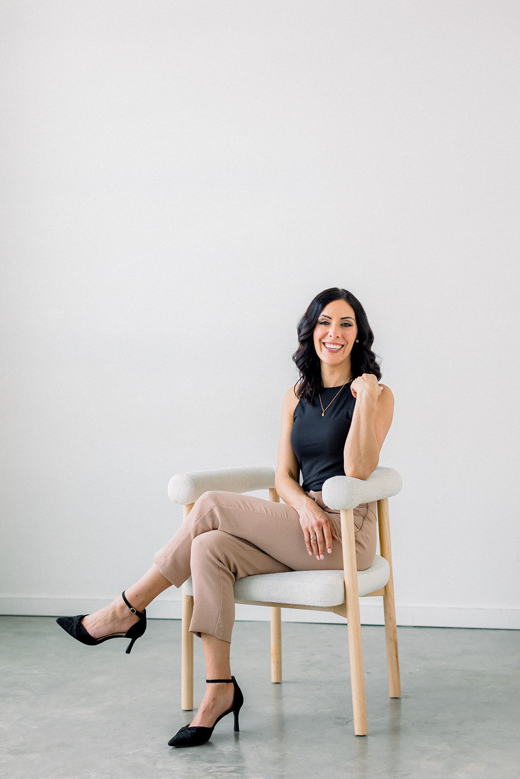 Branding headshot of Calgary business woman with dark hair smiling in a modern white chair.