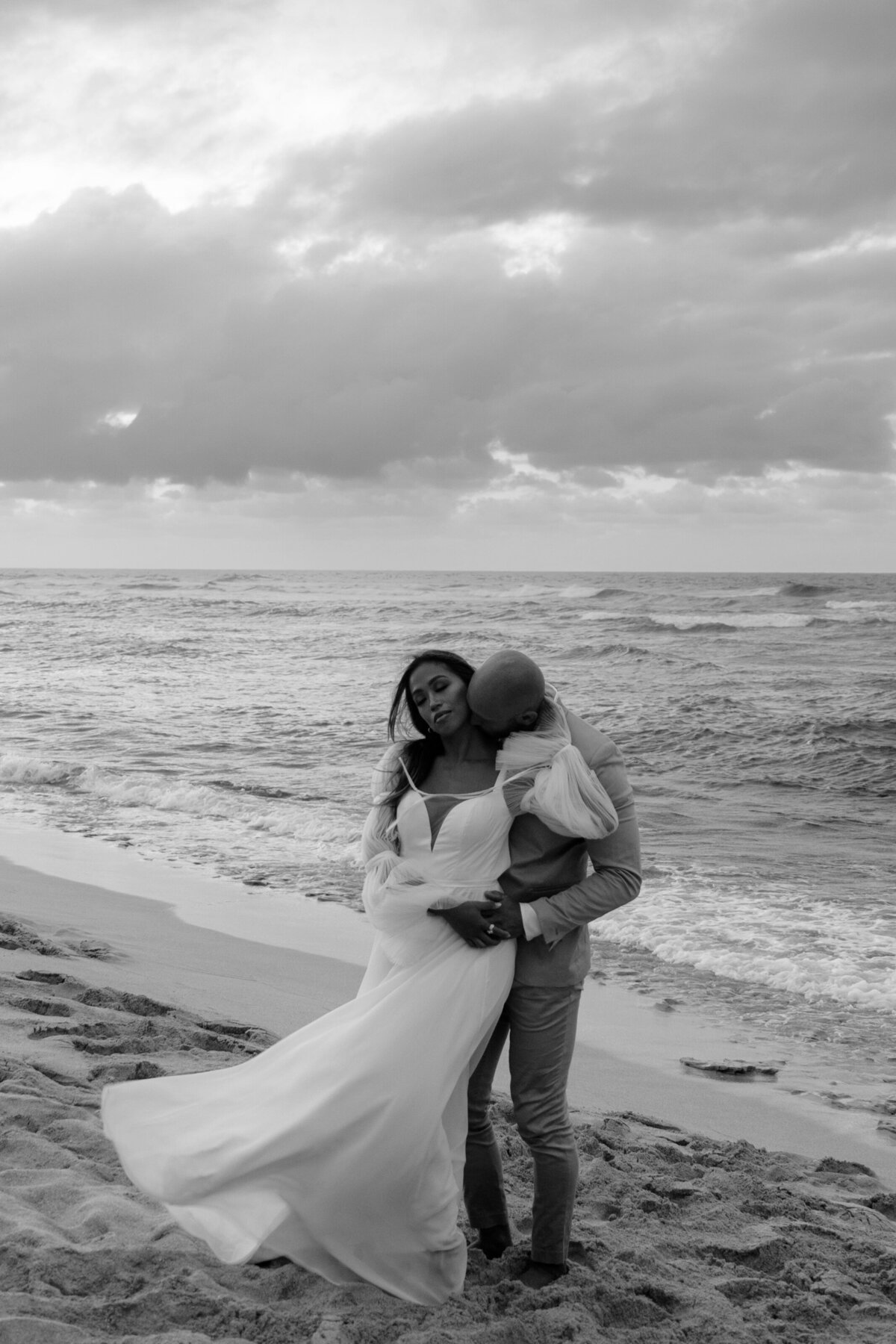 black and white image of bride and groom embracing on the beach