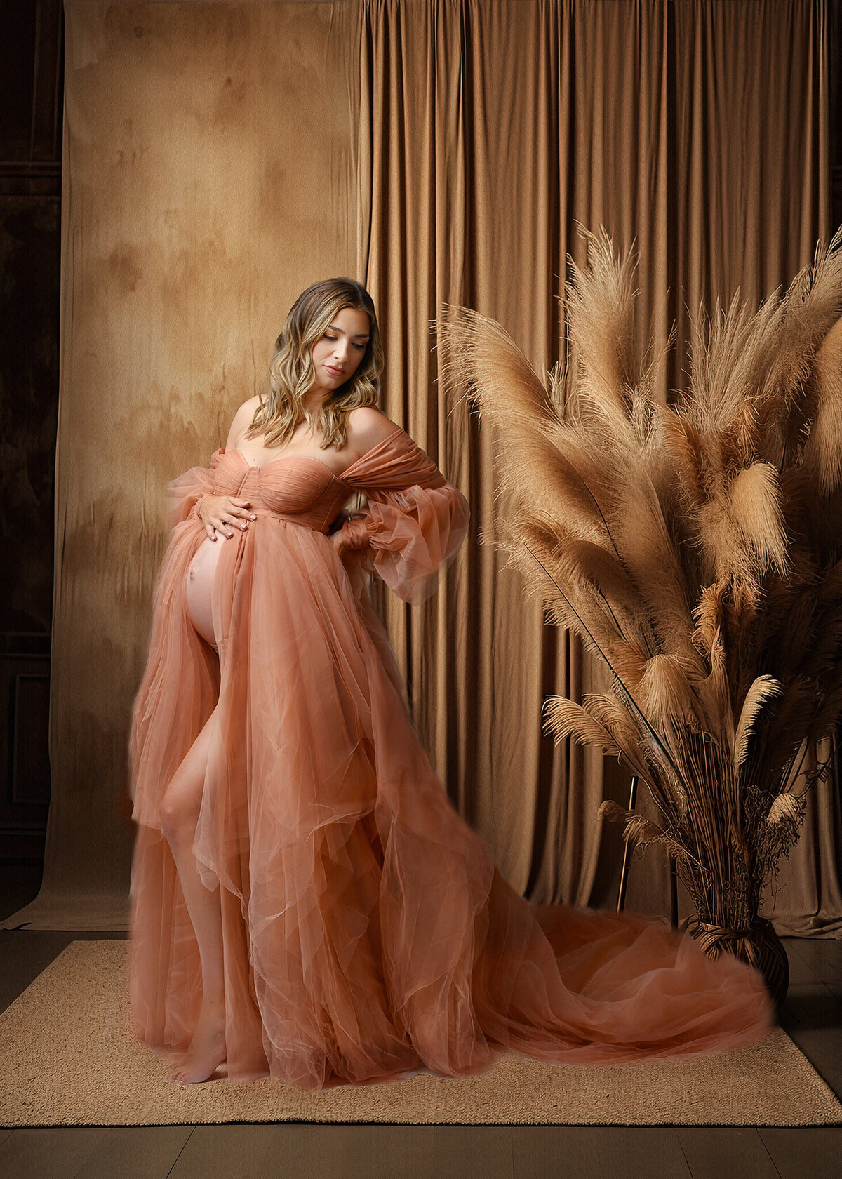Expecting mom in a romantic set up with soft vintage pink gown standing in front of textured wall with golden curtain and dried pampas grass decor