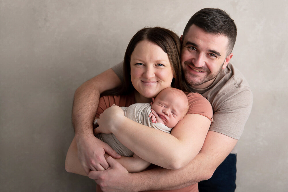 mom and dad cuddling and smiling holding their newborn baby boy.