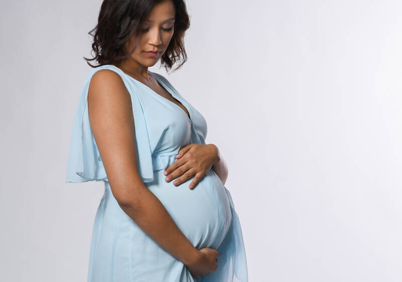 Beautiful pregnant woman looking down at her belly photographed in a blue dress on a white background