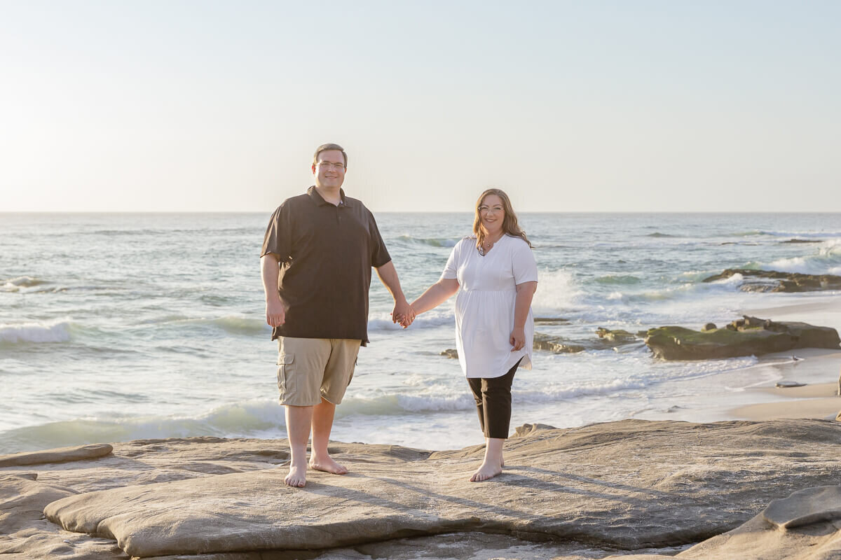Jospeh and Melissa standing on the rocks, holding hands at a beach in La Jolla, California