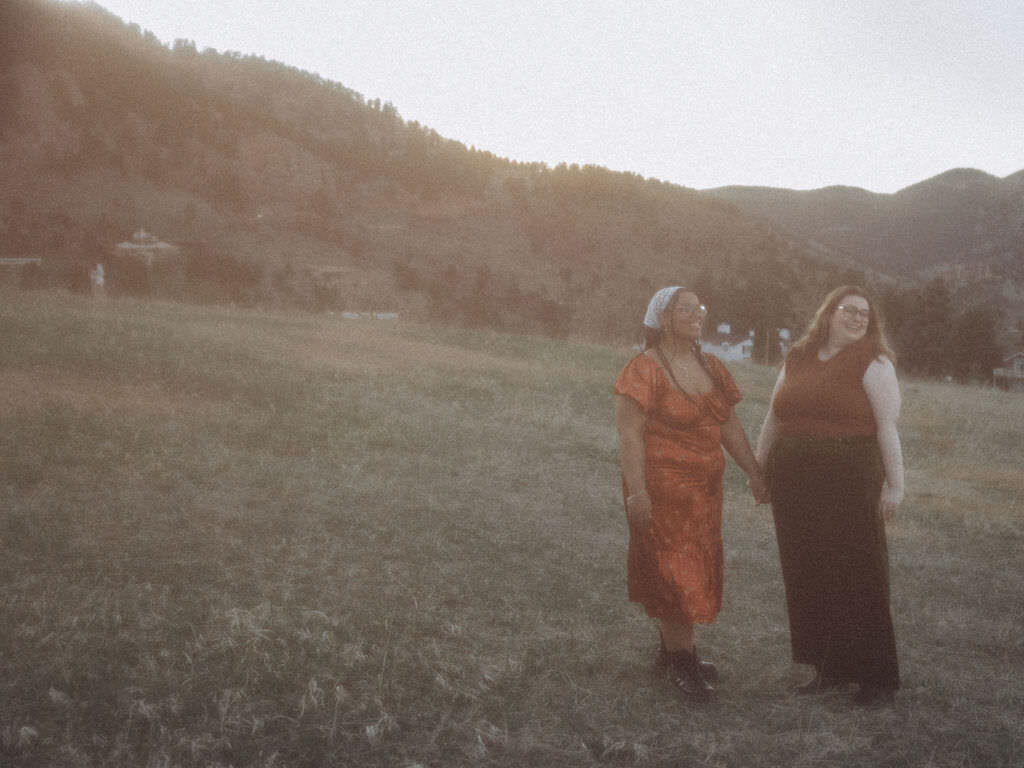 A couple holding hands in a field at sunset.