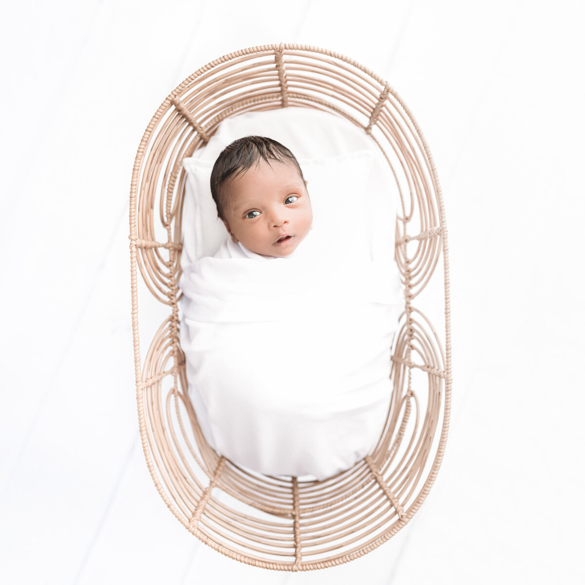Image is of an awake newborn baby in a bamboo bassinet prop. Studio image by Lauren Vanier Photography