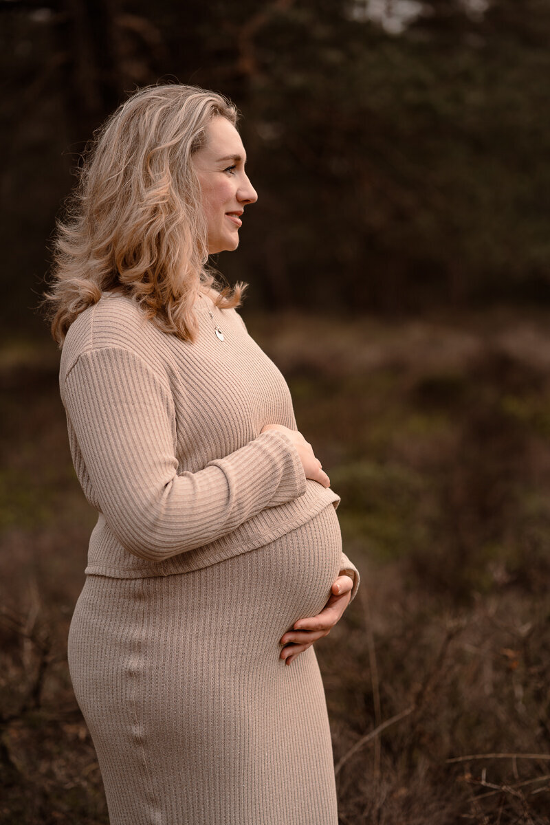Zwangere vrouw heeft haar handen op haar buik en kijkt naar de mooie natuur