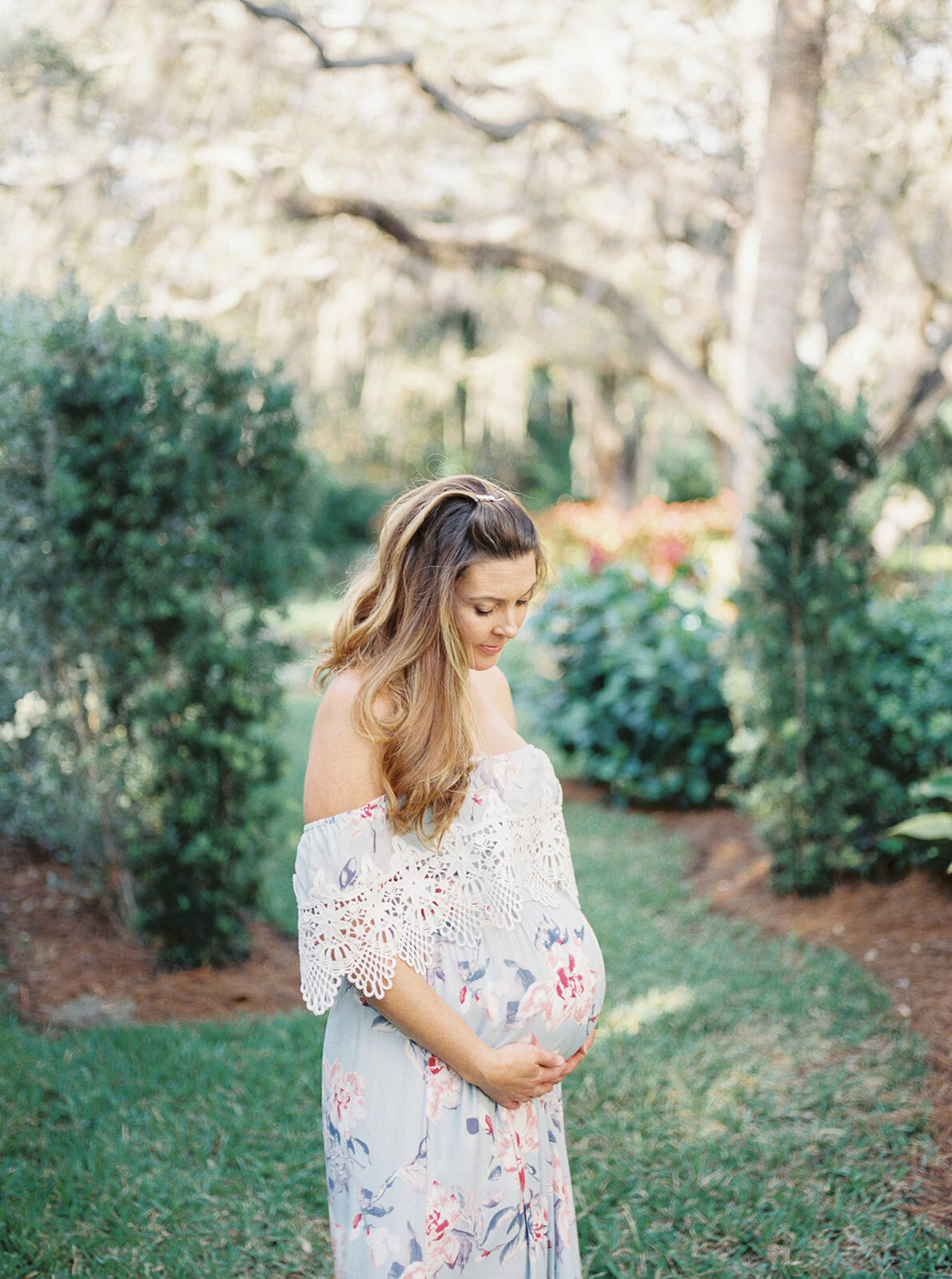 expecting mother cradling belly in floral gown by Orlando maternity photographer.