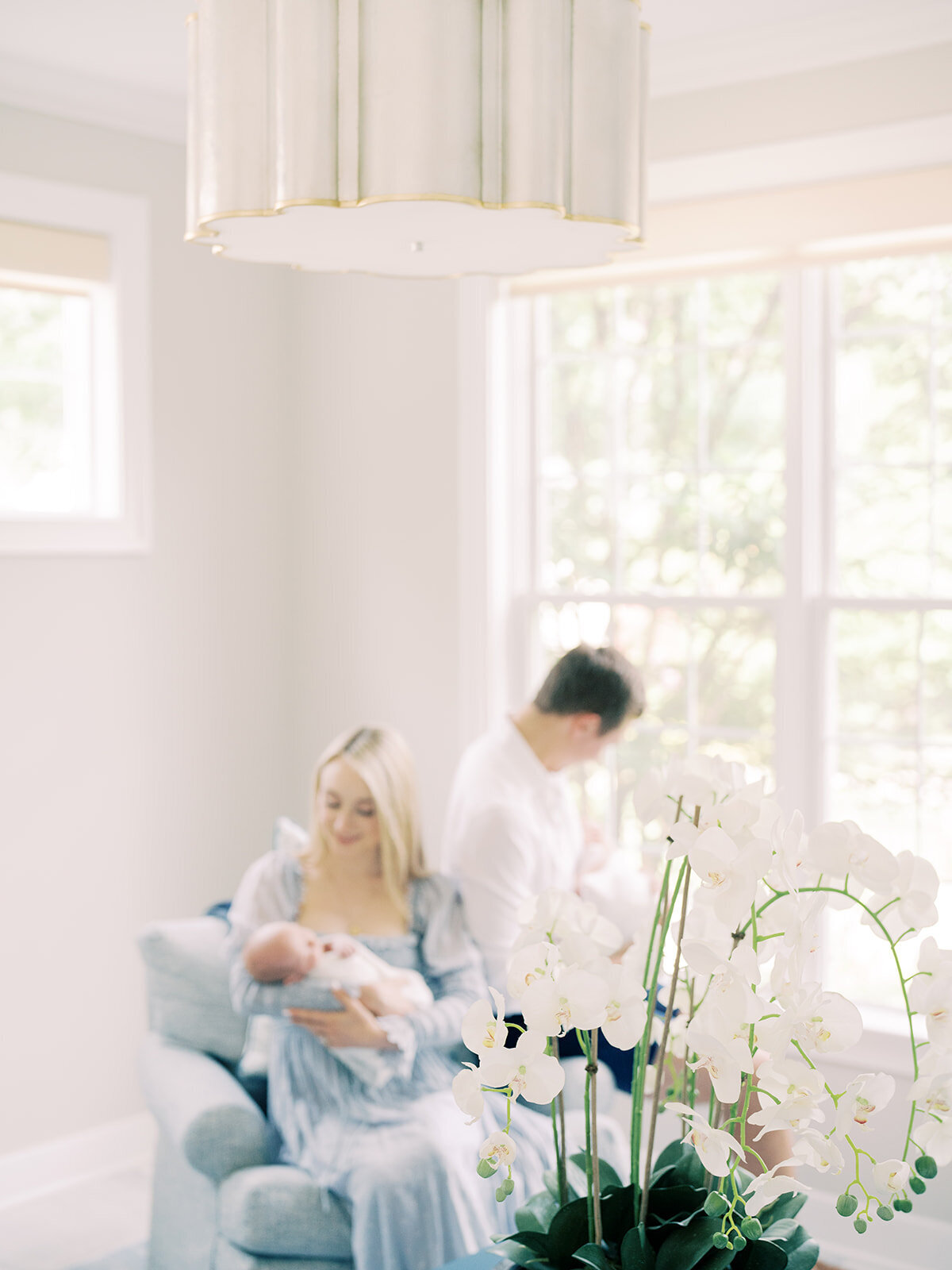 Mother and father sit together in their living room holding their twin baby boys with a white orchid in the foreground.