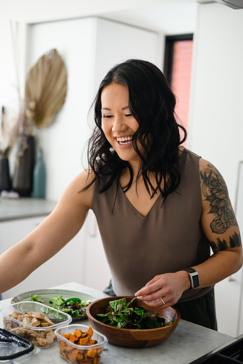 A commercial photographer in Denver takes a photo of an Asian woman standing in the kitchen arranging healthy food for her brand photos and branding photo shoot.