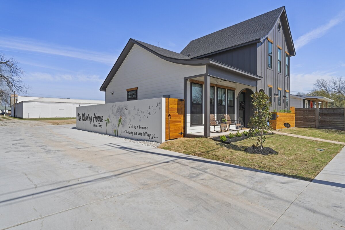 Generous parking area and side view of this two-bedroom, two-bathroom house with wine fridge, firepit, and two master suites located in the heart of the Silo District in Waco, TX.