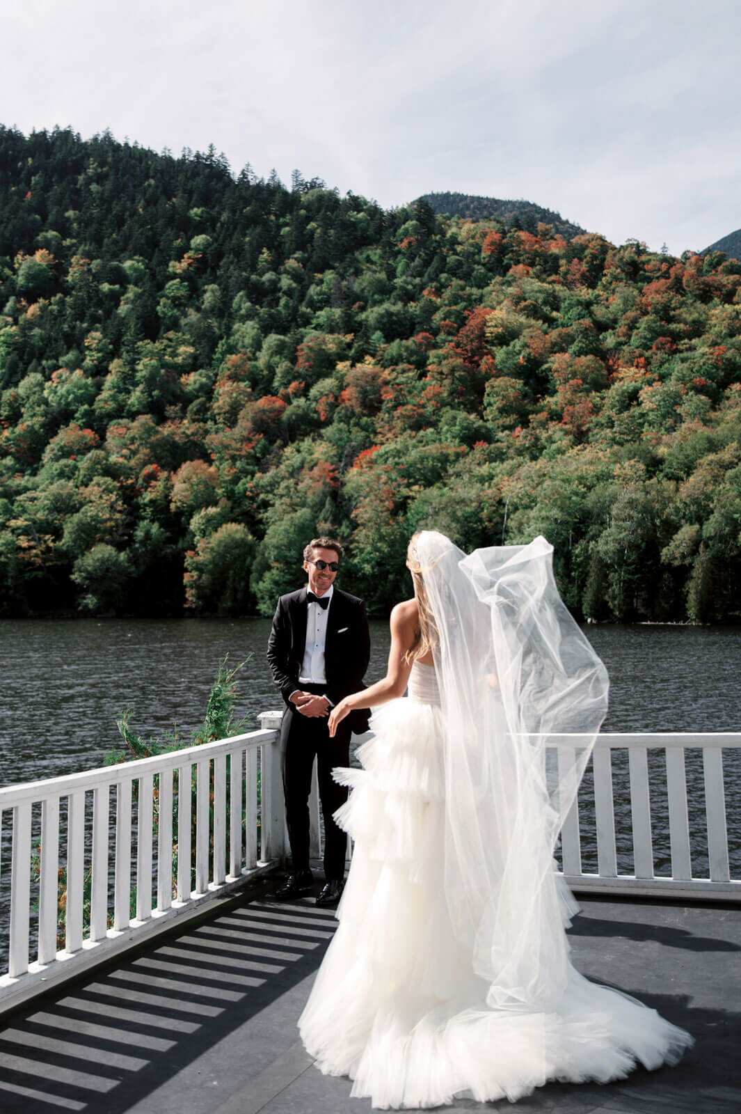 The groom and the bride are facing each other, standing on a terrace, overlooking waters and mountains, at The Ausable Club.