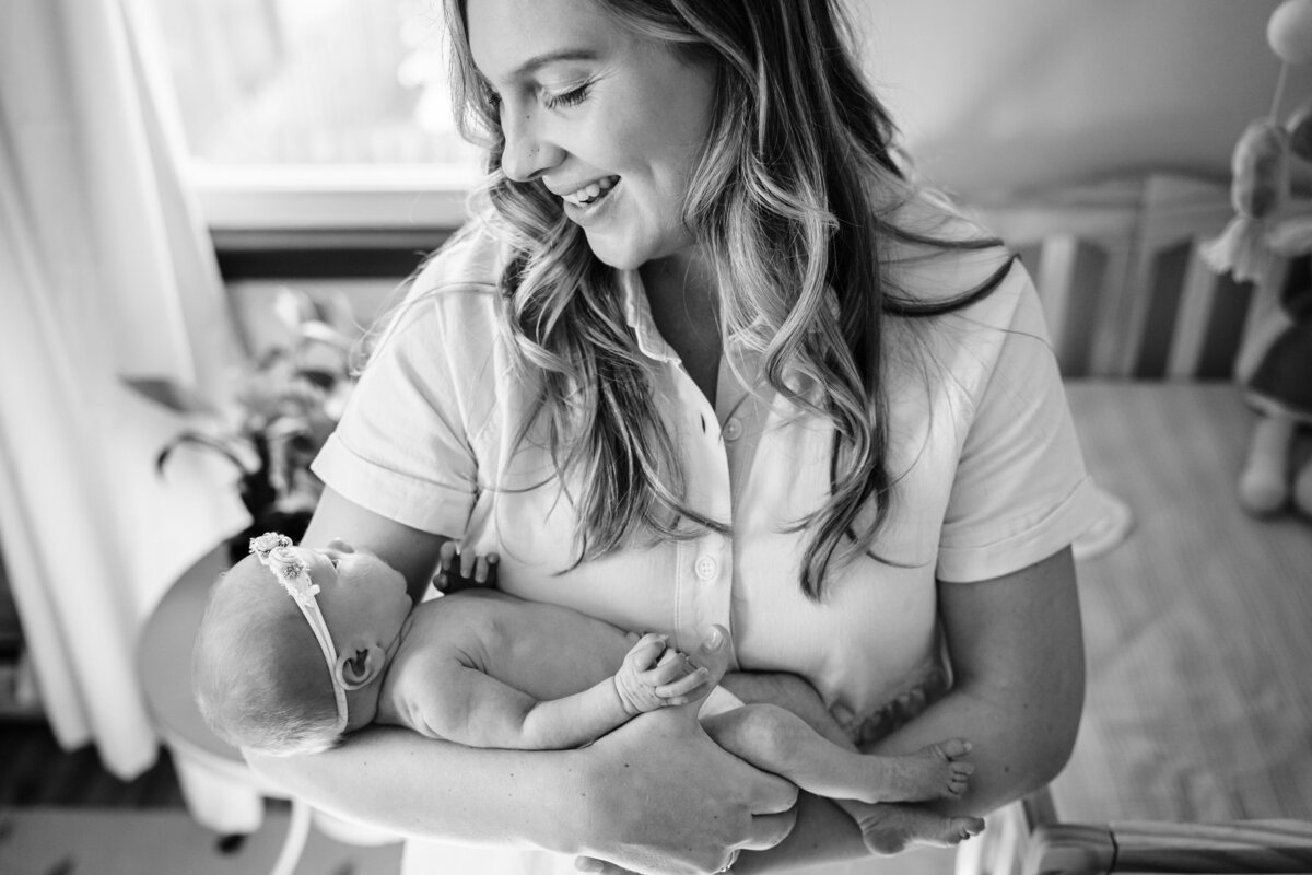 A black and white image of a mother smiling warmly as she cradles her newborn baby in her arms.