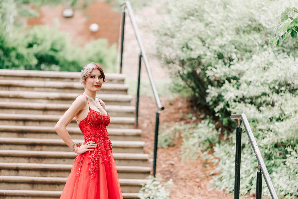 Girl in bright red dress standing by some stairs.