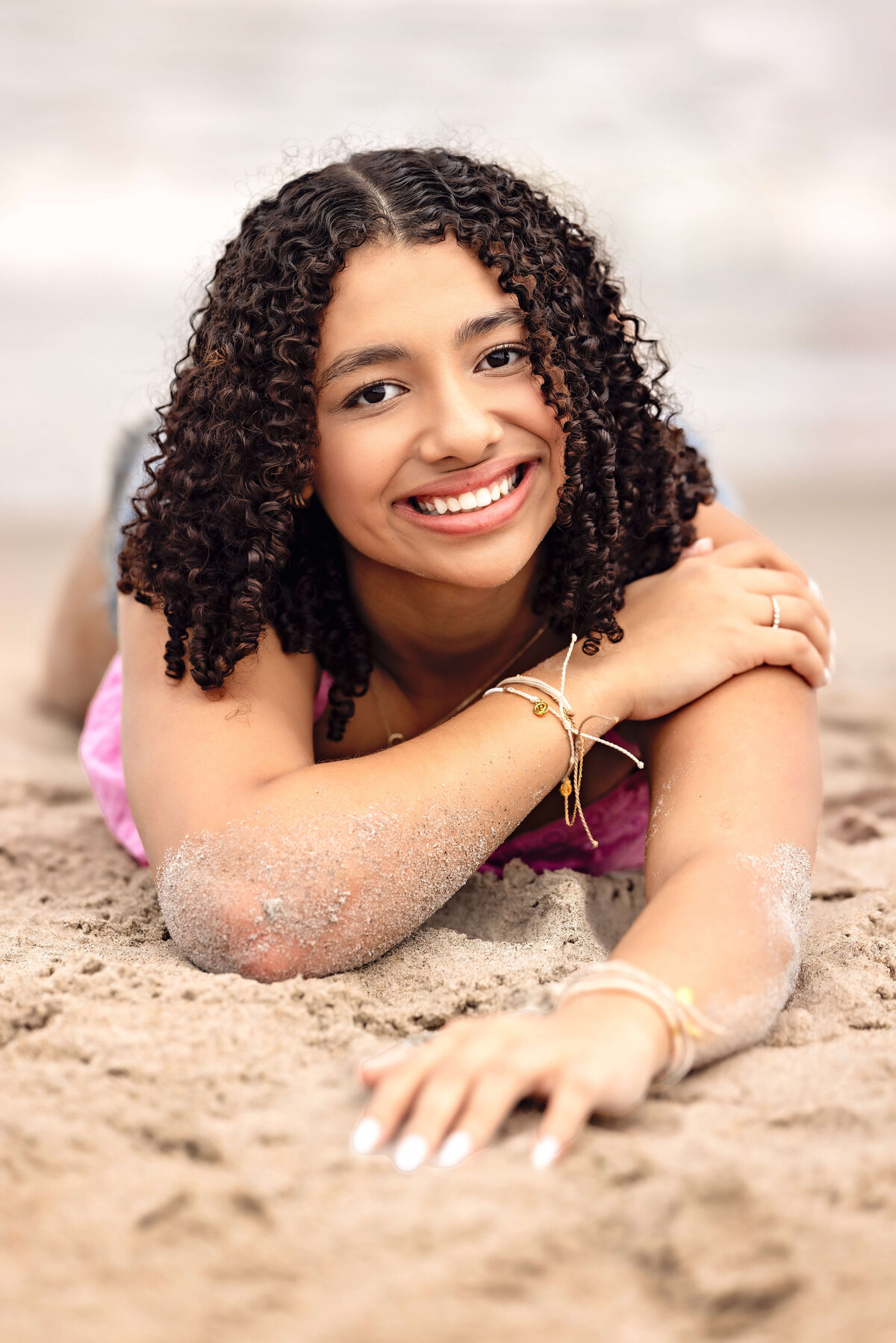 Close-up senior portrait of a girl lying in the sand, one arm stretched out and the other propped under her, ocean grit and gorgeous detail.
