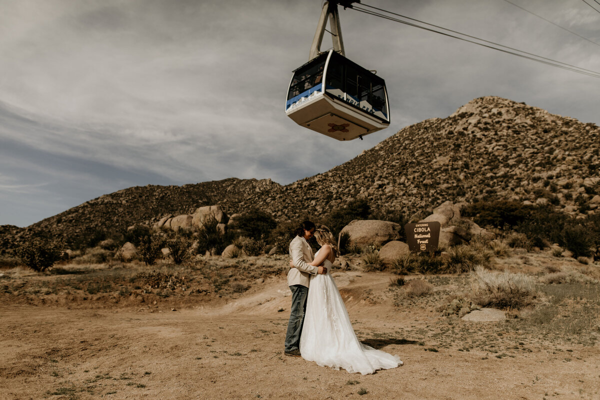 bride and groom standing together with sandia peak tram above them