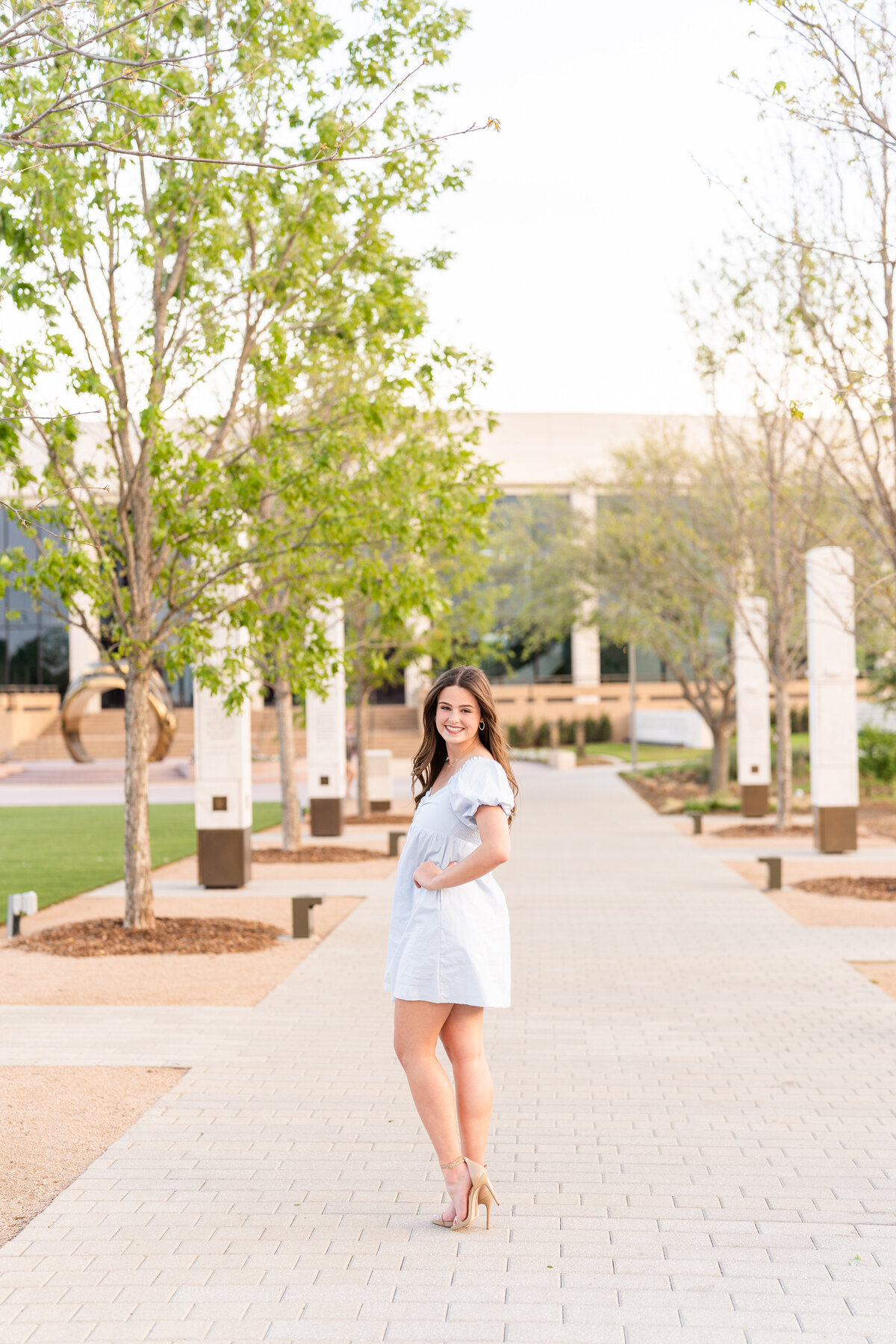Texas A&M senior girl wearing a blue dress with hand on hip and smiling in Aggie Park