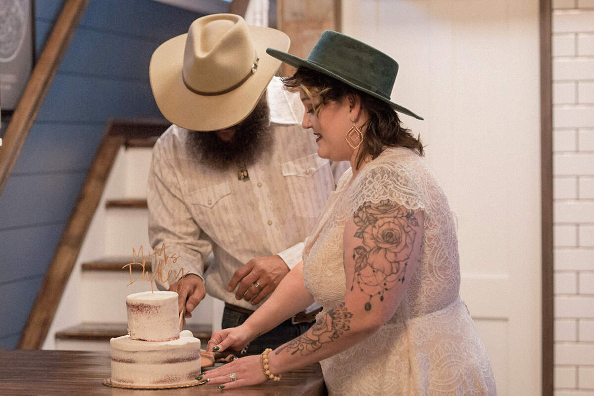 The groom cuts the two layered cake while his bride watches