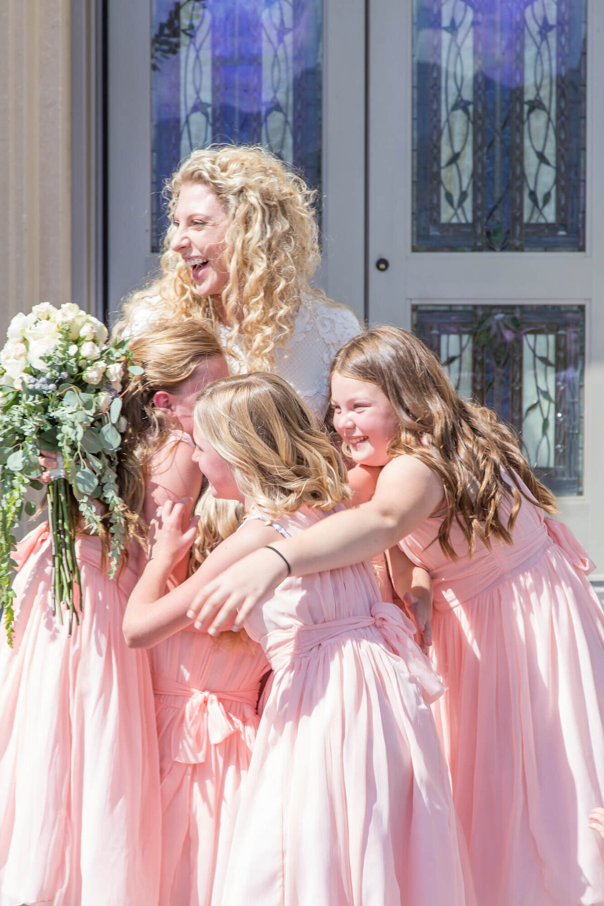 flower girls hugging a bride on a sunny wedding day