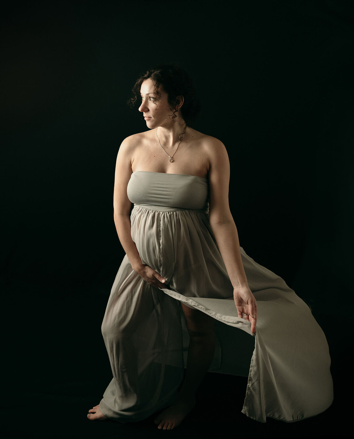 Pregnant woman with gray maternity gown and black background.