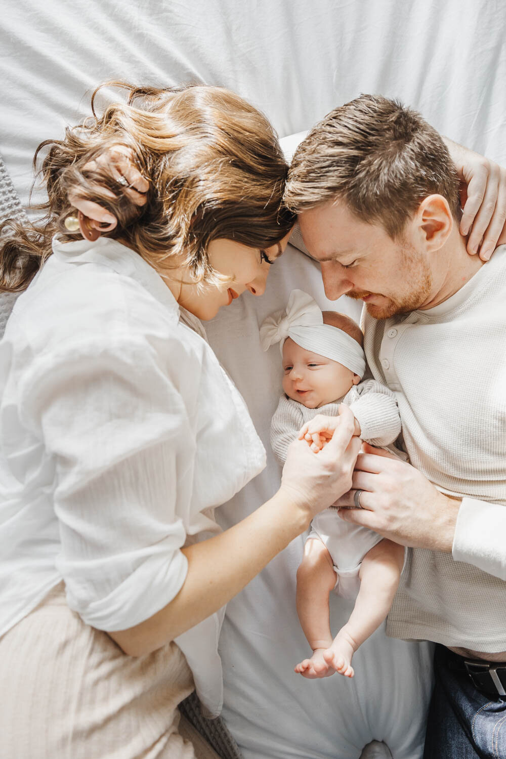 Newborn girl laying between her parents on their bed at their Toronto home