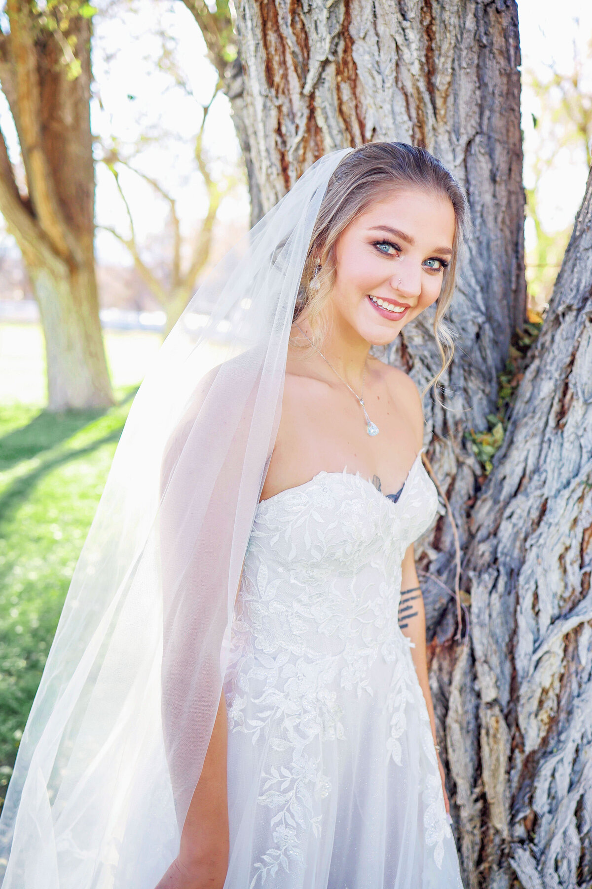 A young bride looking bashfully into the camera, leaning against a tree in aspen, Colorado,