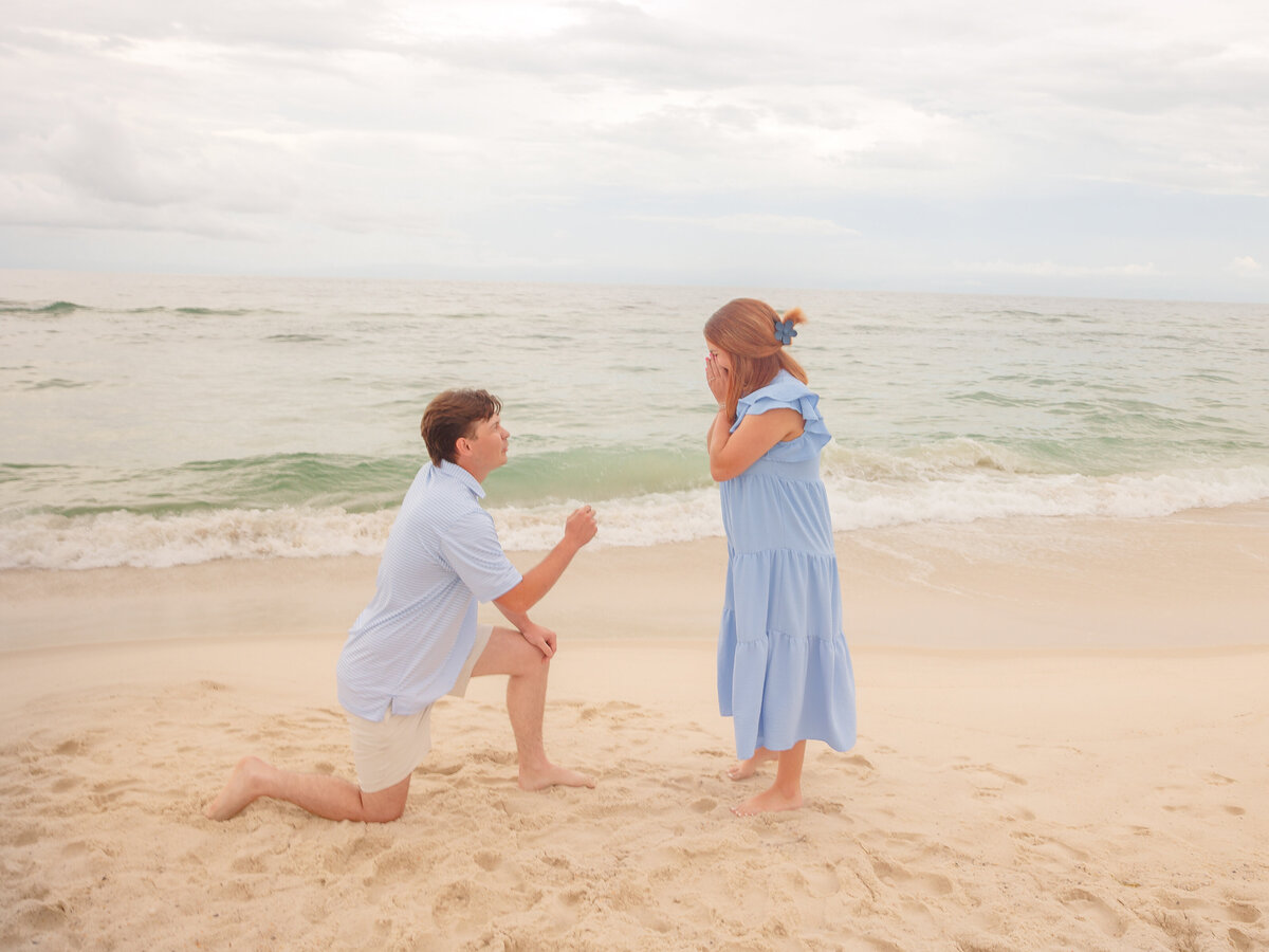 Emotional reaction of a woman covering her mouth in shock during a beachfront proposal in Orange Beach