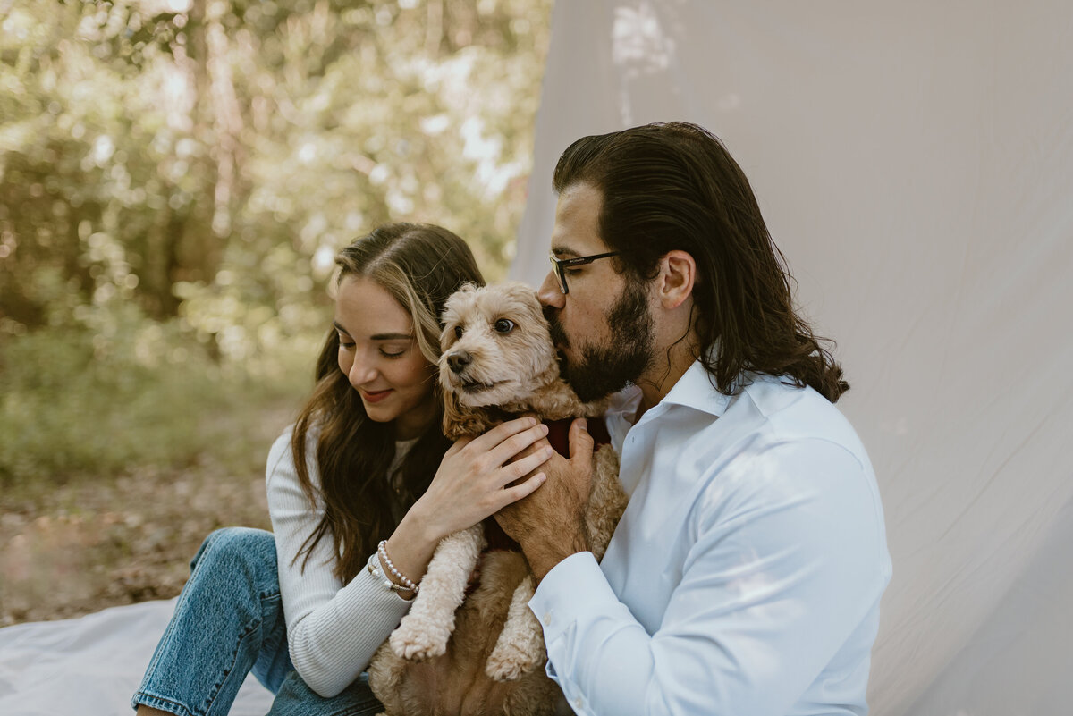 man and woman with their goldendoodle puppy while sitting on a white blanket outside.