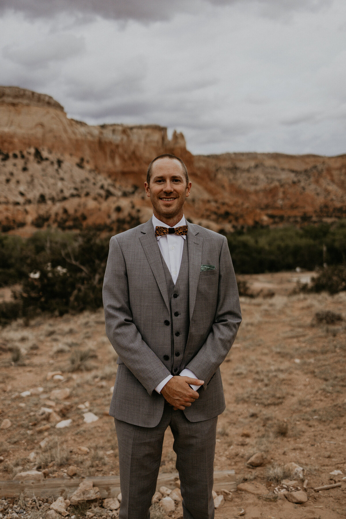 groom smiling in a gray suit in front of red rocks