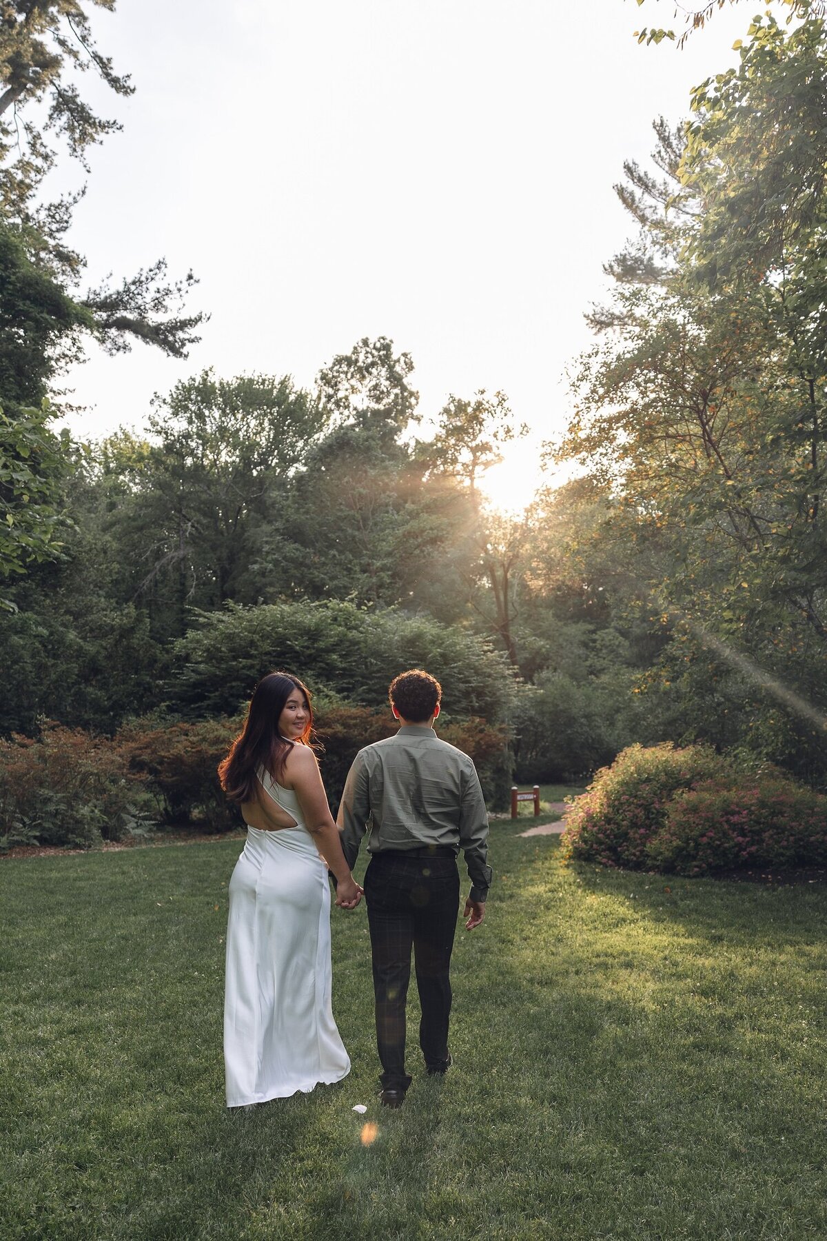 Couple walking hand-in-hand down a wooded garden path.