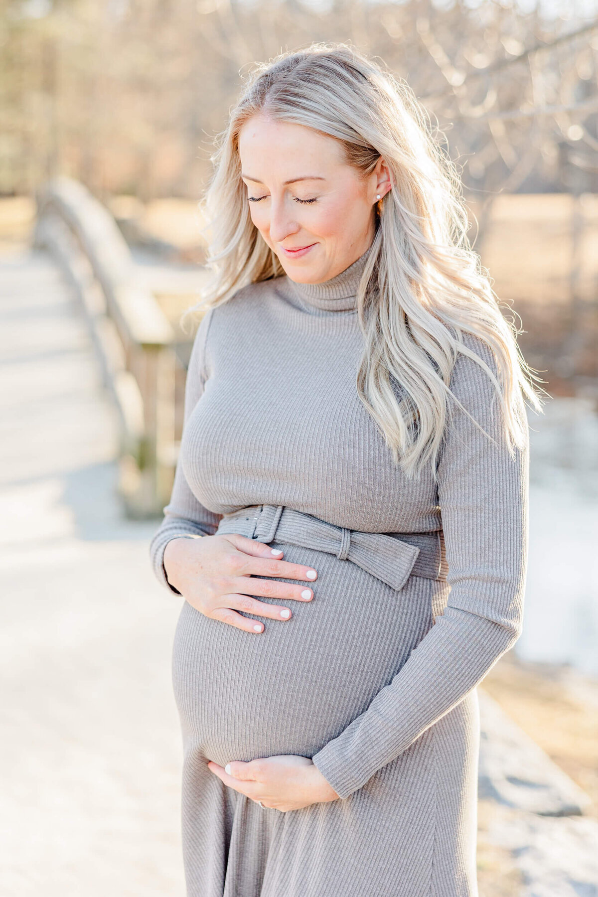 A pregnant woman smiles with her eyes closed in soft light