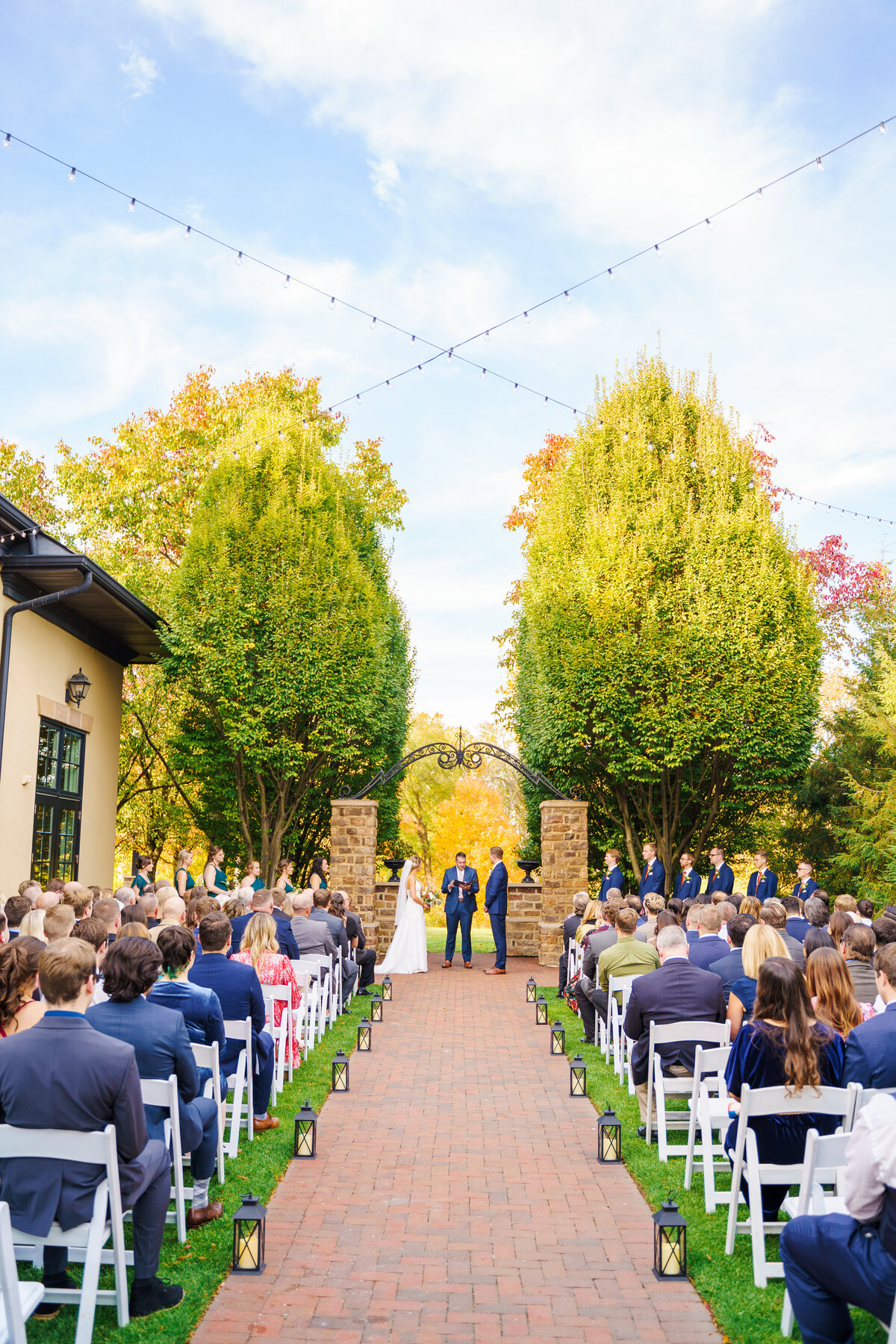 Wedding ceremony with a brick and black metal arch and fall foliage in the background at The Pinnacle Golf Course in Grove City, Ohio.
