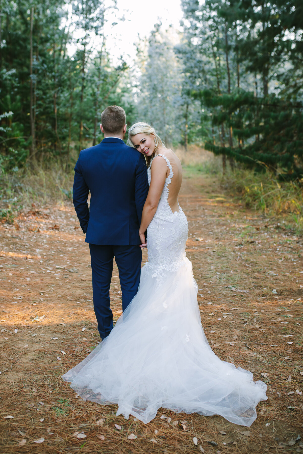 Bride leaning in and holding the groom's arm amongst a pine forest. 