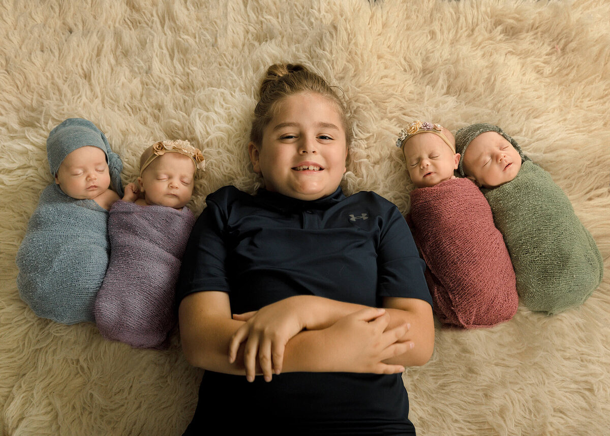Big brother in middle with his quadruplet newborn siblings laying next to him 2 on each side.