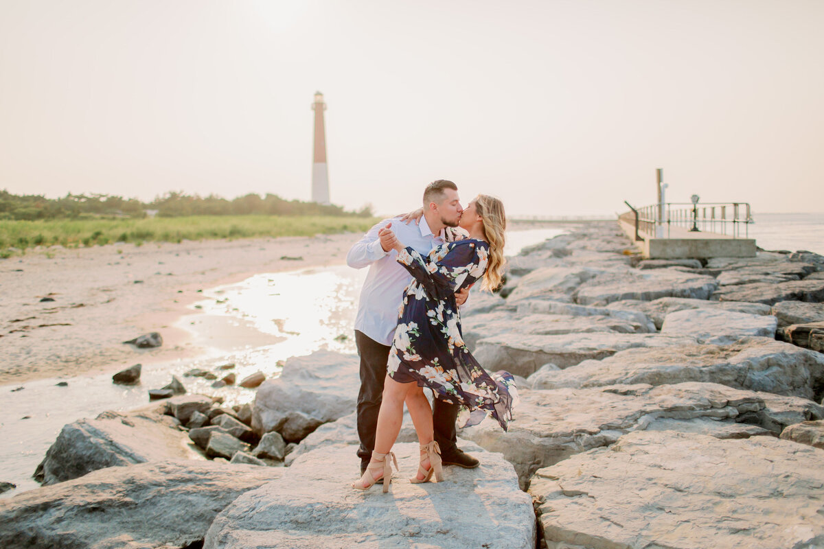 A couple kissing as they stand on rocks of a beach shoreline 