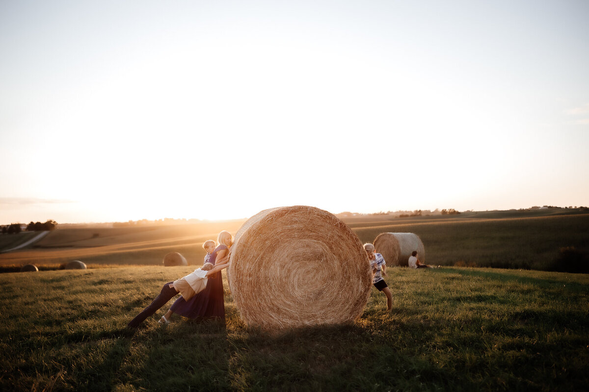 children pushing bale of hay in field of iowa