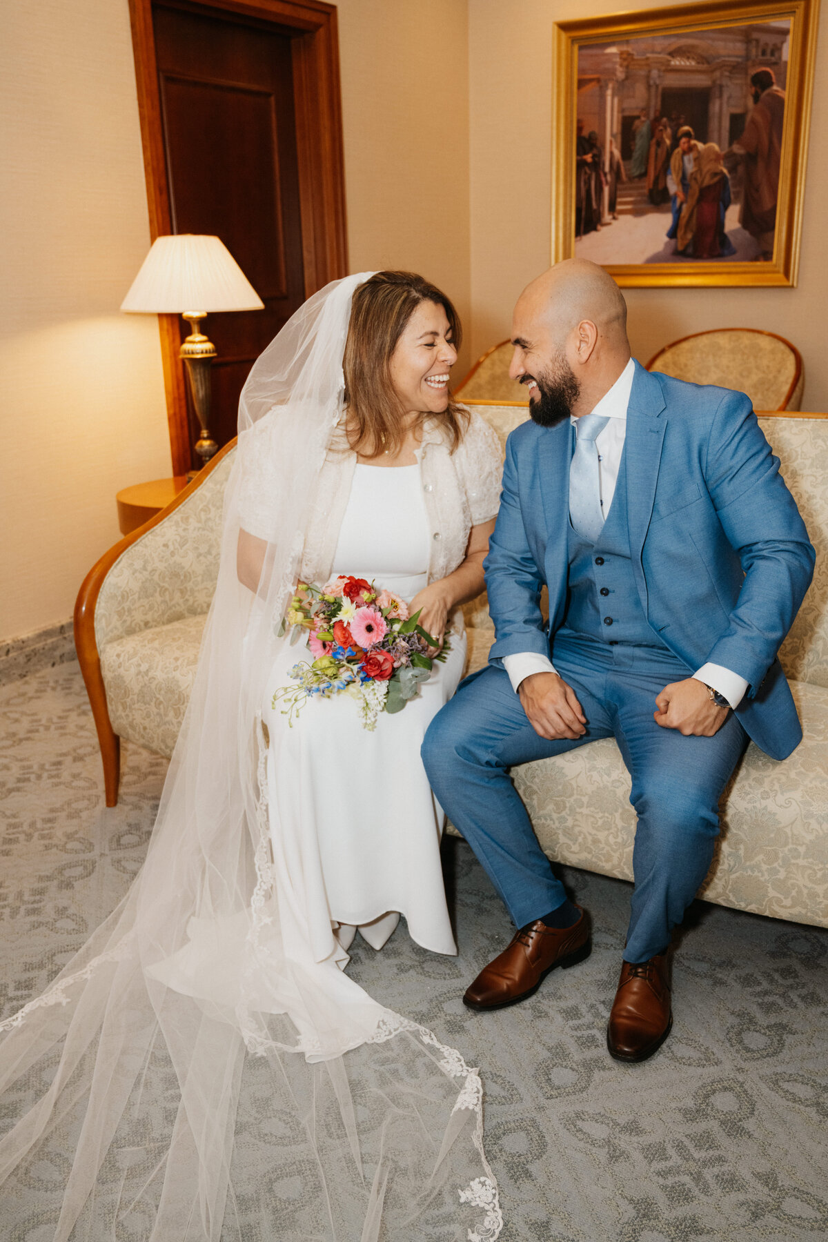 A bride and groom are seated and laughing at each other at The Hague Netherlands Temple after their ceremony