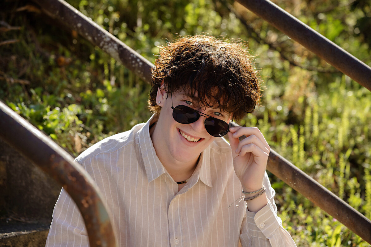 Senior portrait on rusted staircase with industrial textures, featuring a vertical stripe shirt and cream jeans in Charlotte NC.