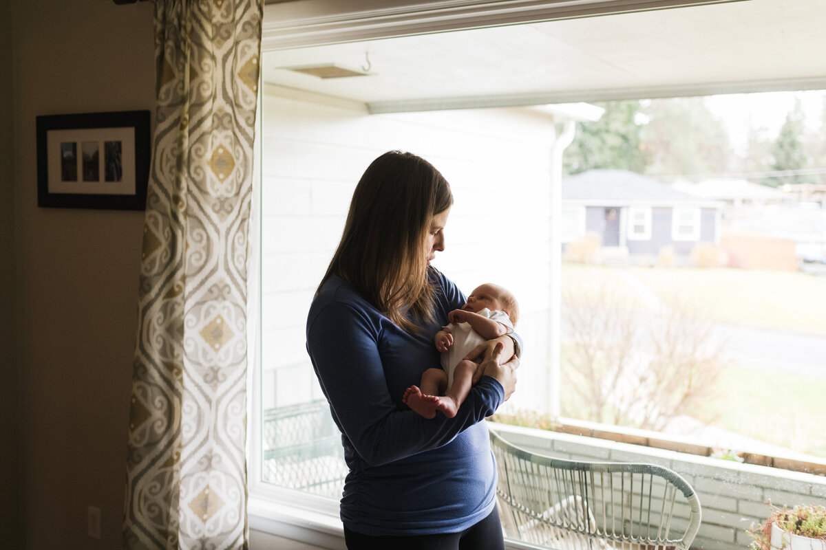 Mom standing with baby by big portrait window