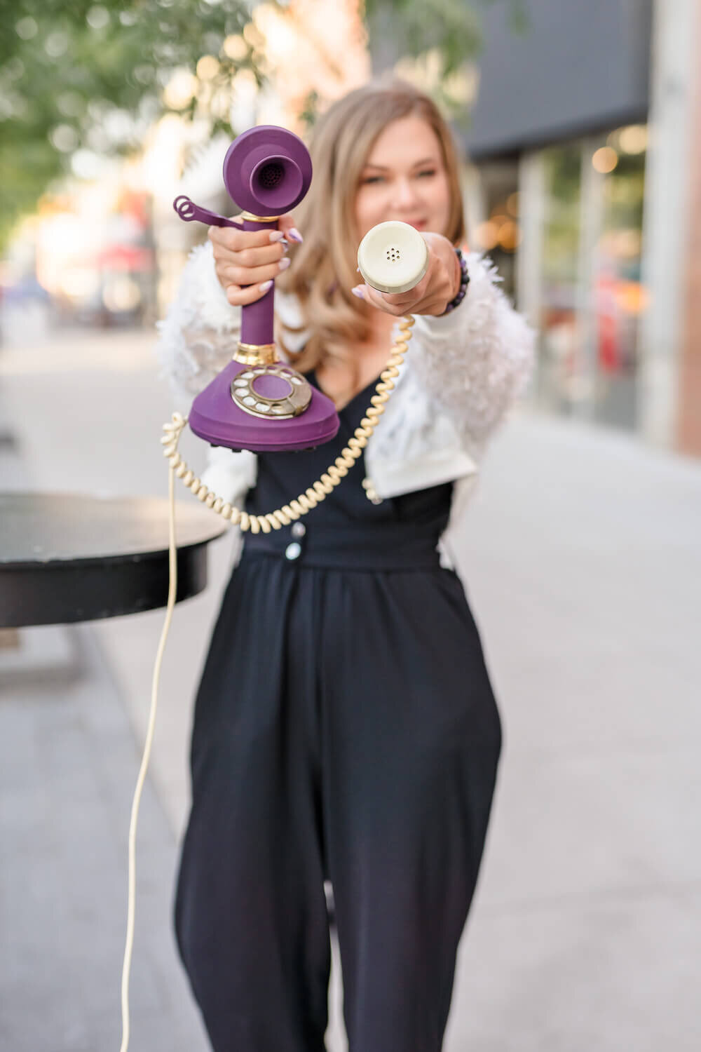 Female coach walking downtown Kelowna holding vintage purple rotary phone towards camera.