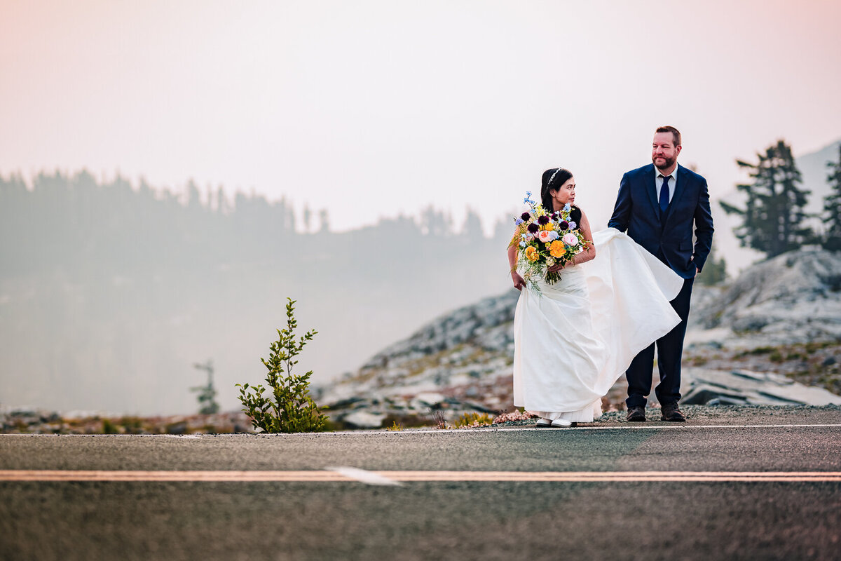 Bride and groom - bride holding flowers and groom holding her dress - both are about to cross a highway in this dramatic and emotive wedding photograph by Maë Lans Photography.