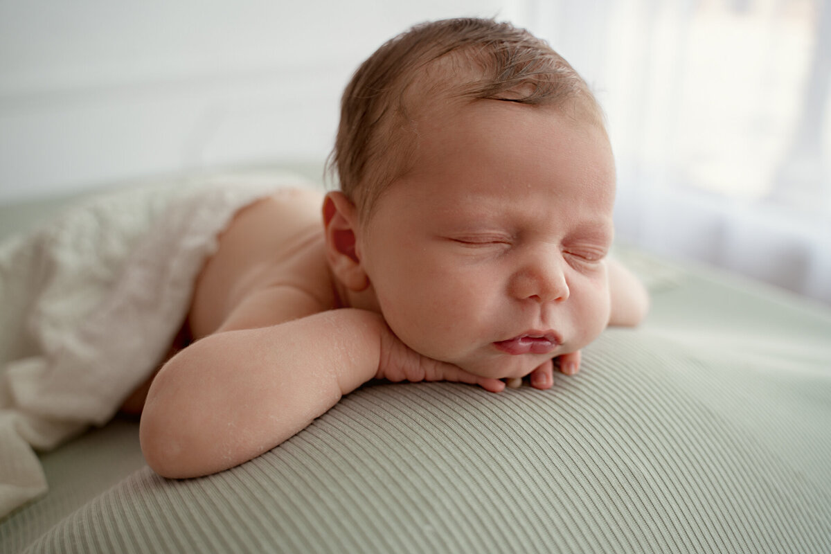 Baby boy on a sage backdrop with his chin on his arms in Dothan, AL