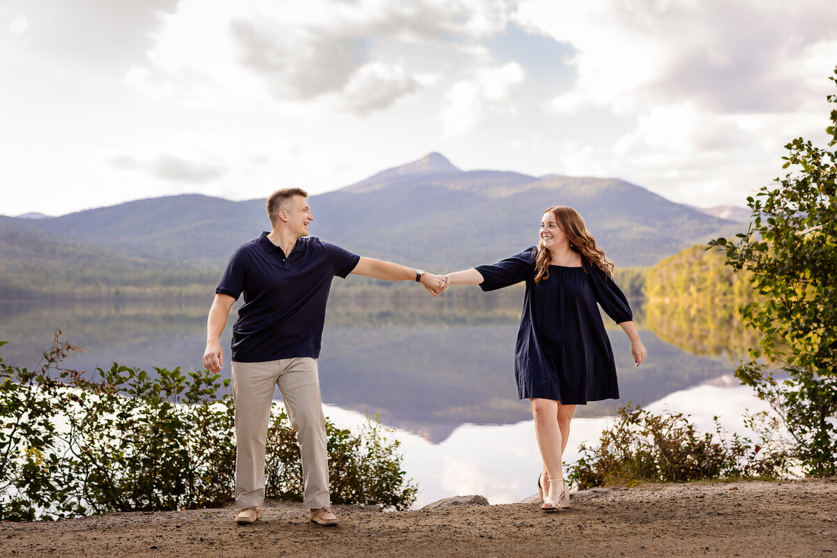 Couple holding hands and walking in front of Chocorua mountain at Chocorua lake celebrating there engagement.