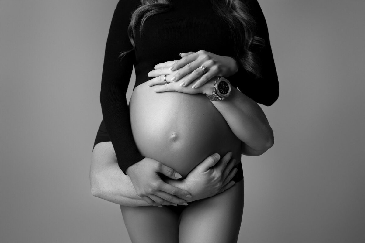 Maternity belly photo with both mom and dad's hands embracing it during a studio session in Austin, Texas
