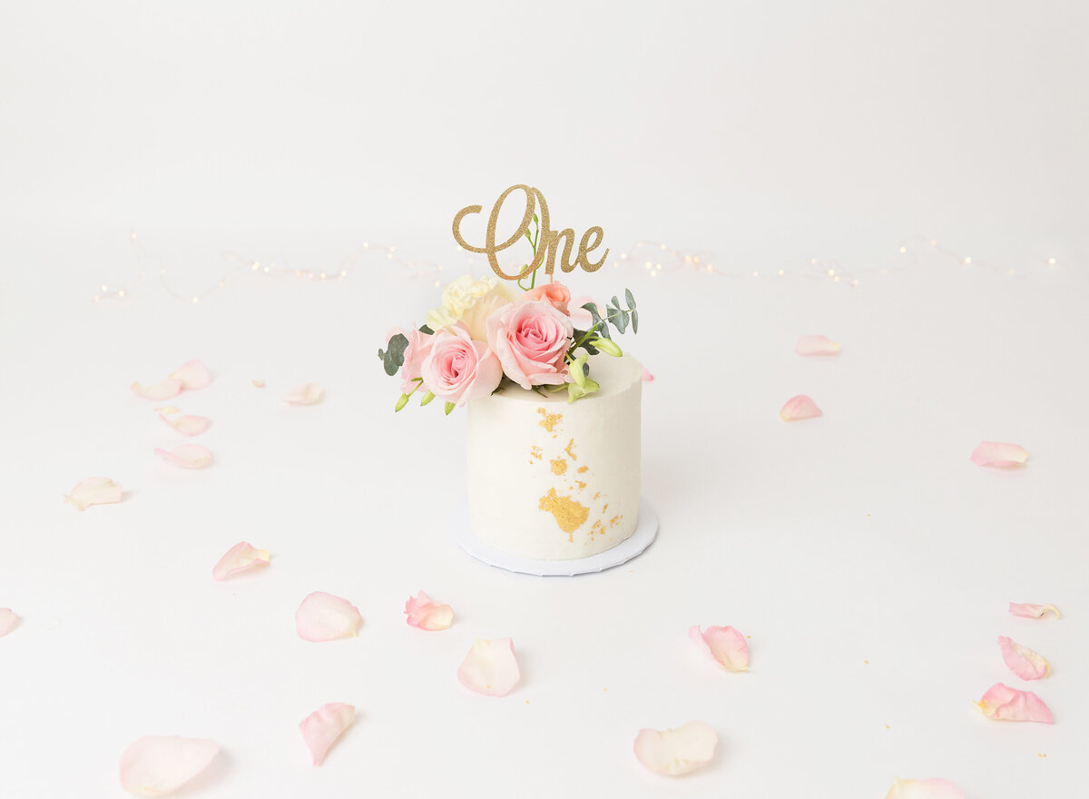 Untouched cake captured before first birthday cake smash. White cake is decorated with gold leaf and fresh flowers.