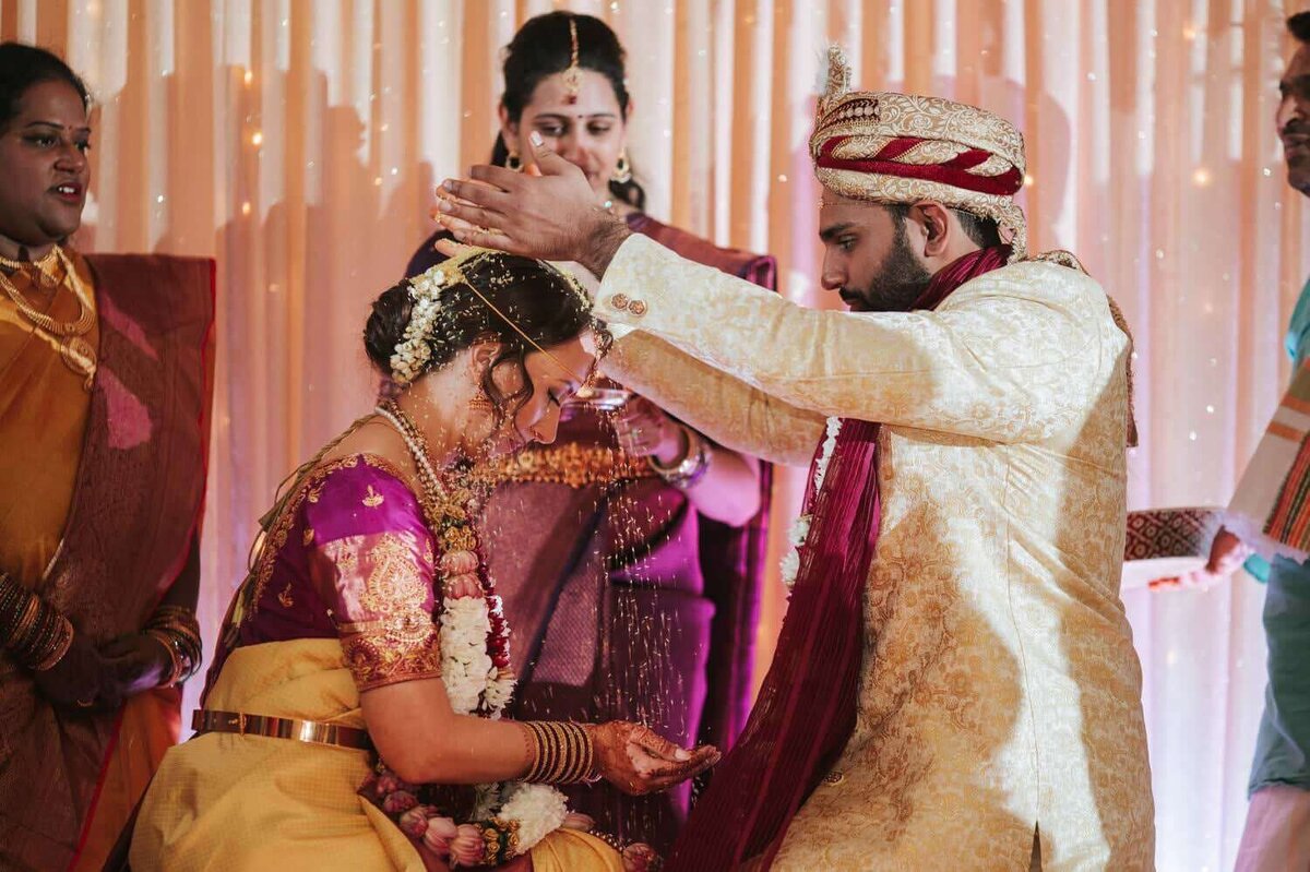 Bride and Groom during their Gujarati Indian wedding ceremony at the Philadelphia Marriott. The bride and groom are poring rice over each other's heads while surrounded by their family under the mundup.