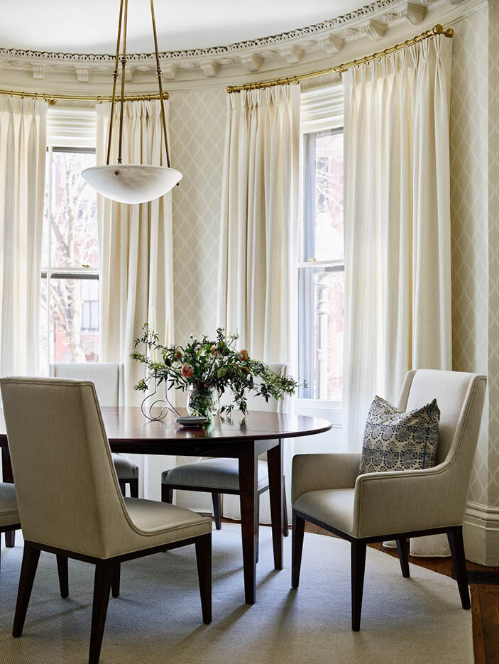 A classic dining room with a curved table, upholstered chairs, trellis wallcovering, linen drapery, and an onyx pendant. Truly timeless. By Sarah Scales.