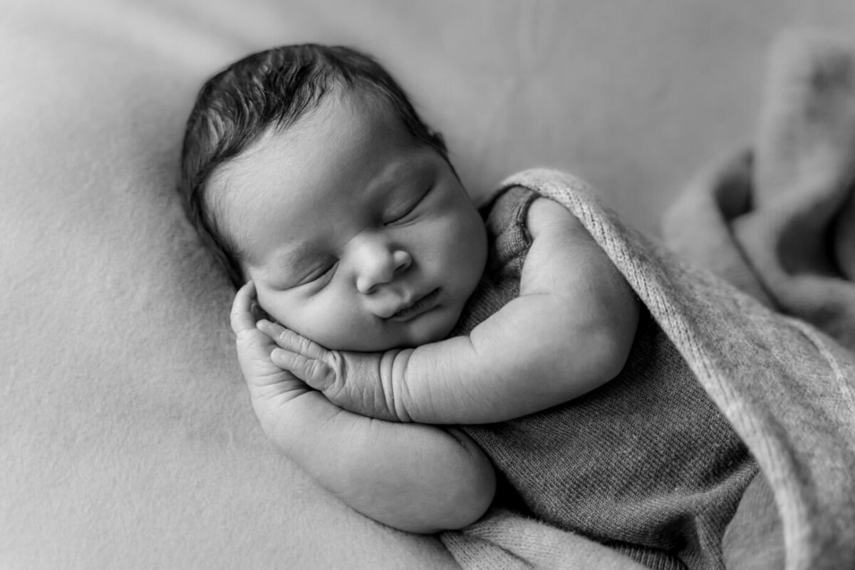 Black and white close-up of a newborn baby sleeping soundly with arms folded under the chin.