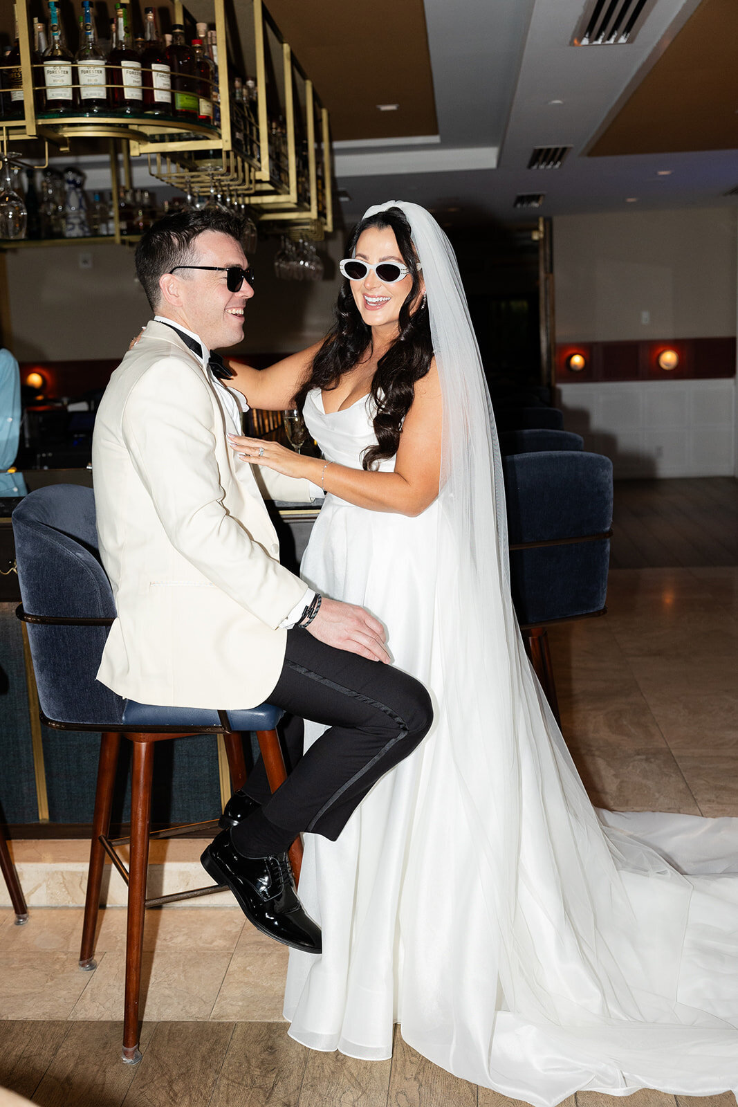 The bride and groom sharing a relaxed moment at the bar, with a chic and playful vibe during their Ocean Reef wedding in Key Largo, captured by Claudia Amalia Photography.